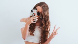 foto van een meisje dat op haar telefoon kijkt en een peace teken maakt